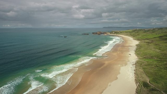 Aerial view sandy beach: ocean foamy waves drops to coastline in White Beach, Antrim County. Seascape of picturesque nature of Northern Ireland. Dramatic summer scenery in day. Footage shot in 4K, UHD