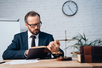 selective focus of bearded lawyer in suit reading book in office