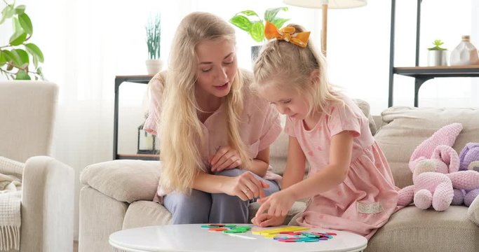 Mother guiding daughter playing and assembling toy blocks at home