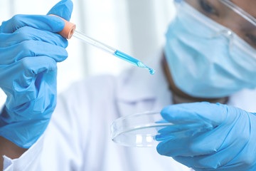 Scientists hand hold the pipette and drop the blue chemical liquid for research and analysis in a laboratory