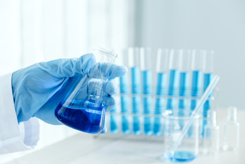 Scientists hold a glass tube filled with blue chemical liquid for research and analysis in a laboratory