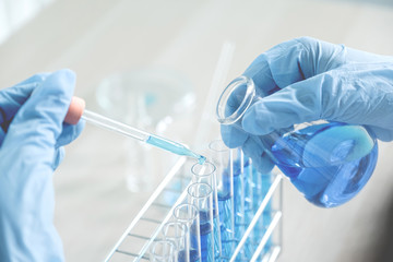 Scientists hand hold glass bottle and the pipette and drop the blue chemical liquid for research and analysis in a laboratory