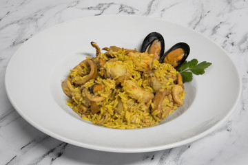 Gourmet seafood presentation. Mediterranean flavor. Paella made with shrimps, squid, scallops, prawns, mussels, saffron and rice in a white dish on the table. 