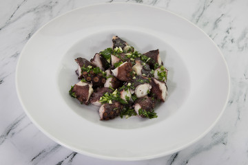 Gourmet food. Mediterranean flavor. Closeup view of an octopus dish with Provencal condiment, made with garlic and parsley.