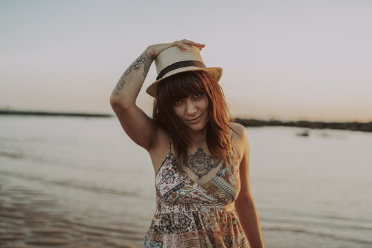Chica joven y guapa con vestido y sombrero paseando por la playa