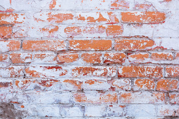Old, antique wall of red destroyed bricks. White plaster was applied to the top of the brickwork. The plaster has peeled off significantly.