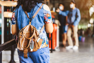 Mini portable alcohol gel bottle to kill Corona Virus(Covid-19) hang on a leather shoulder bag of a woman wear a protective mask at a cafeteria. New normal lifestyle. Selective focus on alcohol gel