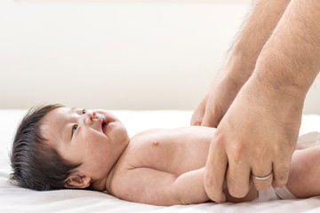 Fototapeta na wymiar シーツの上で横になっている赤ちゃんと、赤ちゃんと手をつなぐ男性の手