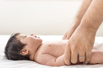 シーツの上で横になっている赤ちゃんと、赤ちゃんと手をつなぐ男性の手
