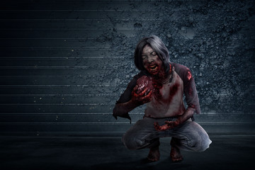 Scary zombie with blood and wound on his body eat the raw meat