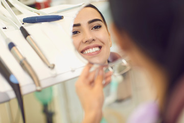Smiling woman looking at mirror at her teeth after dentist visit