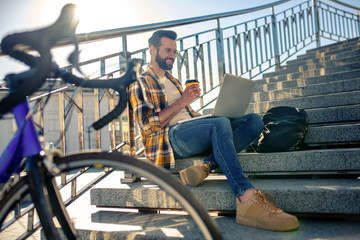 Obraz premium Cheerful man with coffee and laptop on steps
