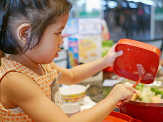 Little Asian baby girl, 4 years old, enjoys putting pork in to a hot pot by herself - engaging baby into food preparation