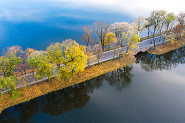 Fototapeta na wymiar picturesque autumn landscape. road through blue lake surrounded by trees with colorful foliage. aerial view from flying drone