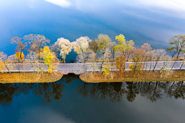 road with yellow and green trees through blue lake. autumn landscape aerial view