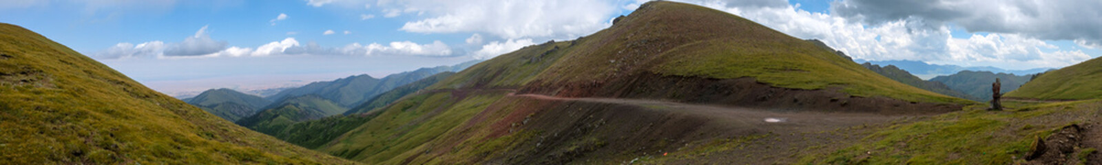 Beautiful panoramic view of green mountains with dangerous gravel road. Ketmen or Ketpen mountains gorge and mountain pass. Tourism in Kazakhstan.