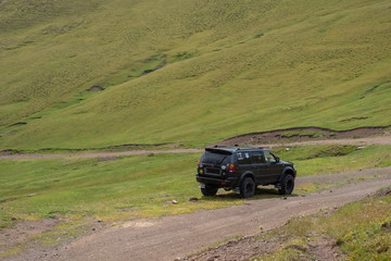 Plakat 4x4 off-road SUV on gravel road in green mountains. Mountain trail landscape. Adventure travel. Ketmen mountain gorge and mountain pass in Kazakhstan. 25.07.2020 Almaty, Kazakhstan.
