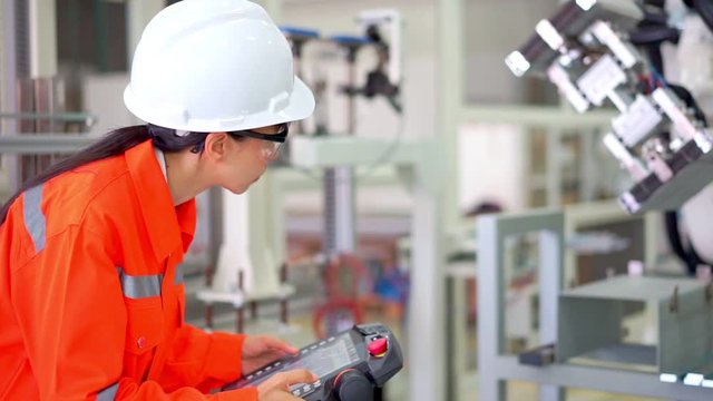 Smart factort concept: An engineer use handheld controller setting industrial robot in production plant.