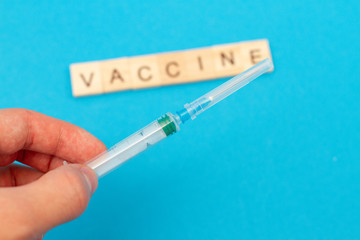 Obraz premium Medical syringe in hand and word VACCINE made from wooden cubes on blue background. Coronavirus. Covid 19 virus. Medical infectious concept