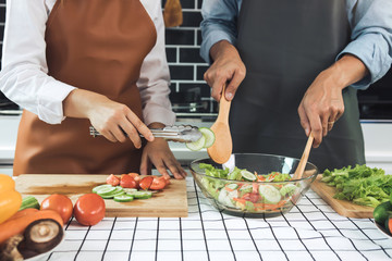 Asian couple preparing healthy salad in the kitchen.