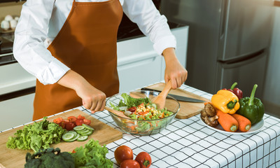Asian woman is mixing the ingredients in a salad bowl at the kitchen cooking table.