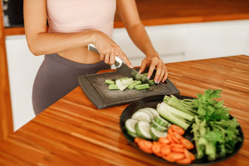 Cropped image woman cutting fresh vegetables on chopping board in kitchen