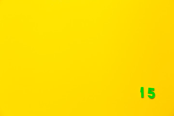 A green plastic toy number fifteen is located in the lower right corner on a yellow background