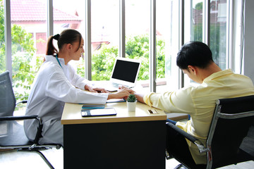 Young Caucasian Female psychiatrist is specialist in psychiatry is checking a pulse on the wrist of asian male Patient and searching results on laptop in Clinical treatment for emotional symptoms.
