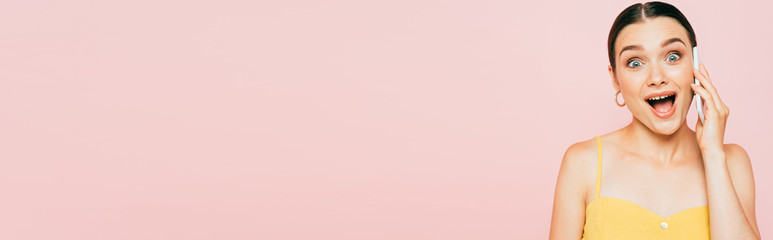 excited brunette young woman talking on smartphone isolated on pink, panoramic shot