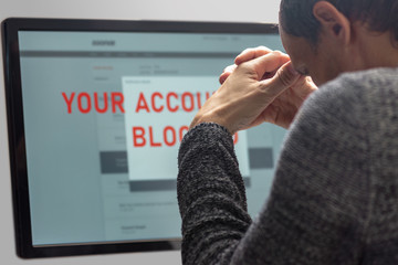 Upset minded man reading text Your account blocked on computer screen