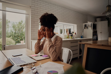 Young stressed woman holding hands on head while sitting in front computer laptop