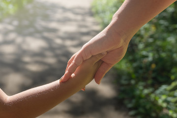 Mother and child hold hands on a walk in the park.