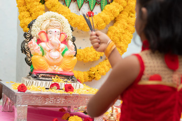 kid praying by closing eyes infront of god Ganesha idol by holding or offering incense in hand during ganapati festival celebration at home.