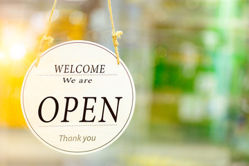 Text on white sign board  “Welcome  we're open" infront of the glass shop with the boken yellow and green bright background.
