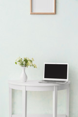 Table with laptop near white wall in room