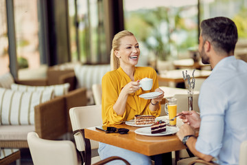 Happy woman drinking coffee and talking to her boyfriend while relaxing in a cafe.