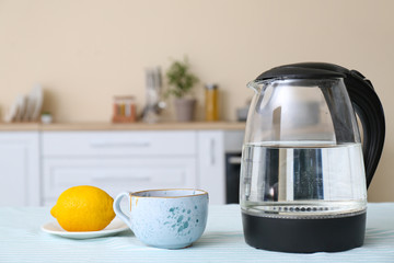 Electric kettle, cup of tea and lemon on kitchen table