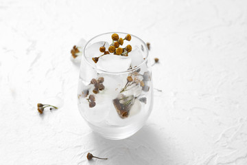 Glass with frozen flowers in ice on white background