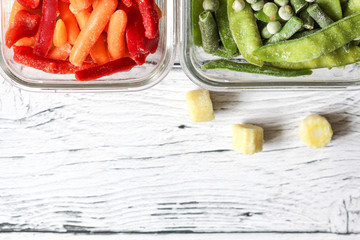 Frozen vegetables such as green peas, pea pods, green beans, red sweet pepper and baby carrot in the transparent bowls on the concrete wooden background with copy space, top view