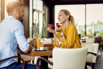 Cheerful woman eating donut and talking to her boyfriend in a cafe.