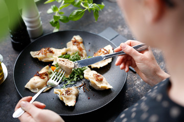 Dumplings. The woman is eating dumplings. Traditional homemade meat dumplings served on a black plate. Suggestion to serve the dish. Top view.