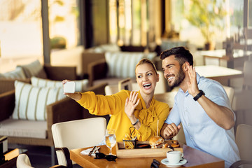 Happy couple taking selfie with smart phone while eating in a restaurant.