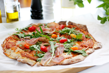 Thin crust pizza. Traditional Italian pizza with Parma ham, cherry tomatoes and arugula.