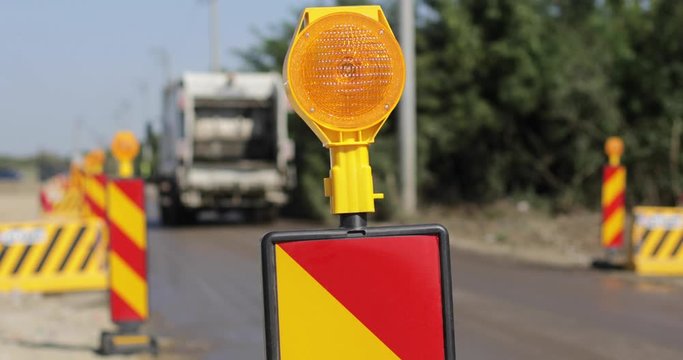Shallow depth of field footage with road warning lights on a construction site and a garbage truck passing by.