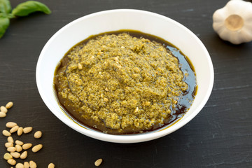Homemade Basil Pesto with Parmesan and Pine Nuts on a black background, side view.