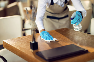 Close-up of waitress disinfecting tables in a cafe. - obrazy, fototapety, plakaty
