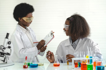 Two african american cute little boy and girl student child learning research and doing a chemical experiment while making analyzing and mixing liquid in test tube at science class on the table