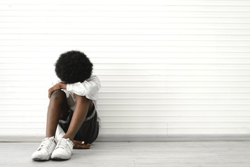 Portrait of sad depressed black african american cute little boy child alone sitting on floor at...