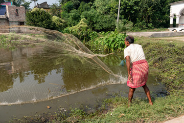 A village fisherman is throwing the net for fishing in a pond