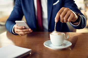 Fototapeta na wymiar Close-up of businessman having cup of coffee while using smart phone in a cafe.